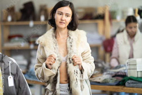 Canvas Print Woman customer is trying on fur jacket next to skin during shopping in store, examining reflection in mirror