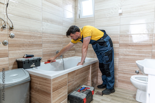 Plumber repairing bathtub in contemporary bathroom during daytime