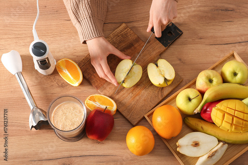 Young woman cutting fresh fruits for smoothie in kitchen