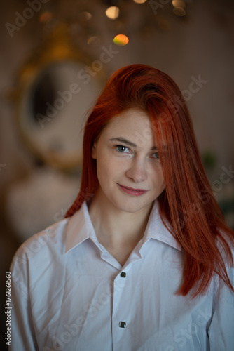 A cute red-haired girl in a white blouse smiles sweetly