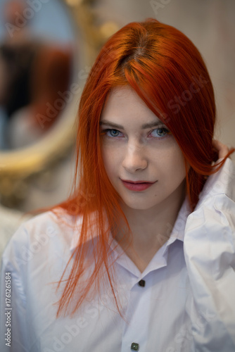 A beautiful red-haired girl smiles charmingly and cunningly, playing with her hair and playing with her eyes or making eyes at someone