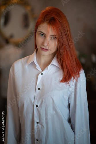 A beautiful girl with long red hair in a white formal classic shirt or blouse