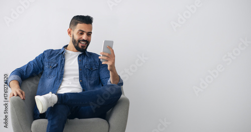 Vászonkép A man enjoys using his smartphone while seated comfortably in a modern chair