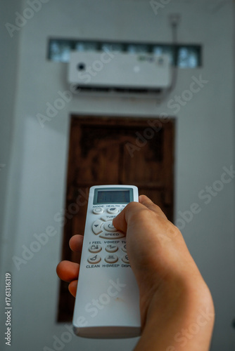 view of a hand holding the AC remote control with the AC mounted on the wall.