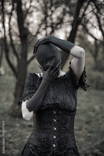 A creepy monster or the ghost of a witch woman with blackened hands and a face wrapped in black bandages in an antique dress with a corset. The Forest witch or the spirit