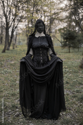 A creepy monster or the ghost of a witch woman with blackened hands and a face wrapped in black bandages in an antique dress with a corset. The Forest witch or the spirit