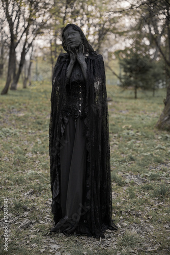 A creepy monster or the ghost of a witch woman with blackened hands and a face wrapped in black bandages in an antique dress with a corset. The Forest witch or the spirit