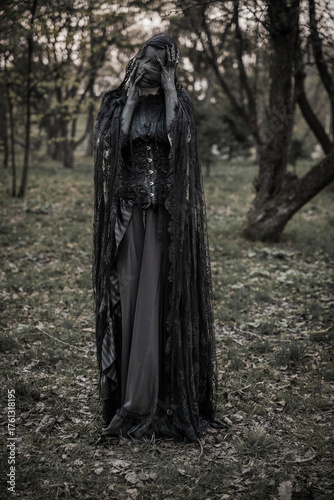 A creepy monster or the ghost of a witch woman with blackened hands and a face wrapped in black bandages in an antique dress with a corset. The Forest witch or the spirit