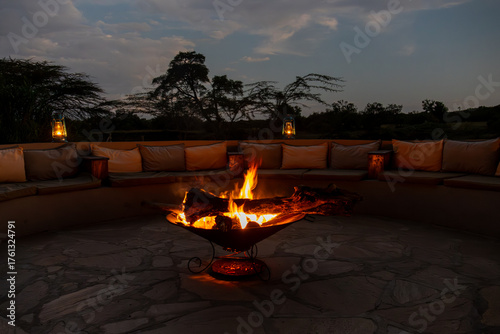 A cozy fire pit burns brightly, surrounded by comfortable seating in an outdoor lounge area at dusk