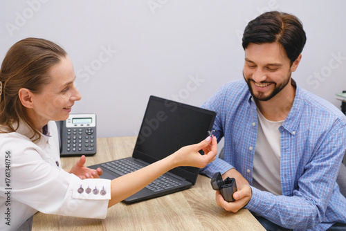 Foto Otolaryngologist showing Modern miniature hearing aids for mid aged man at modern medical center