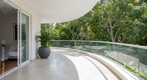 A serene covered balcony with a plant boasts lush tropical foliage views beyond the glass railing.