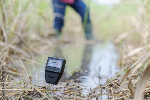 A soil pH and moisture meter inserted in wet farmland ground during flooding, showing smart farming tools used for environmental monitoring and soil quality analysis in agricultural fields.