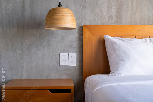 Modern hotel room design with comfortable bed, bedside table and industrial style concrete wall.