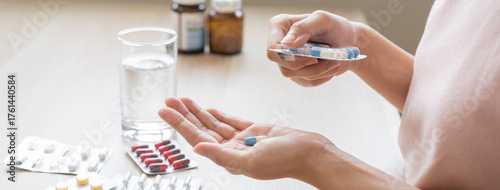 Foto Sick ill asian young woman, girl hand taking tablet pill capsule out from blister pack, painkiller medicine from stomach pain, head ache, pain for treatment, take drug or vitamin at home, health care