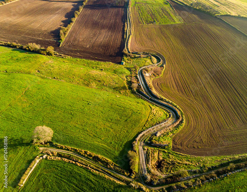 High-quality aerial photo showcasing a distinctive zigzagging stone path cutting across organized, green farmland or agricultural fields.