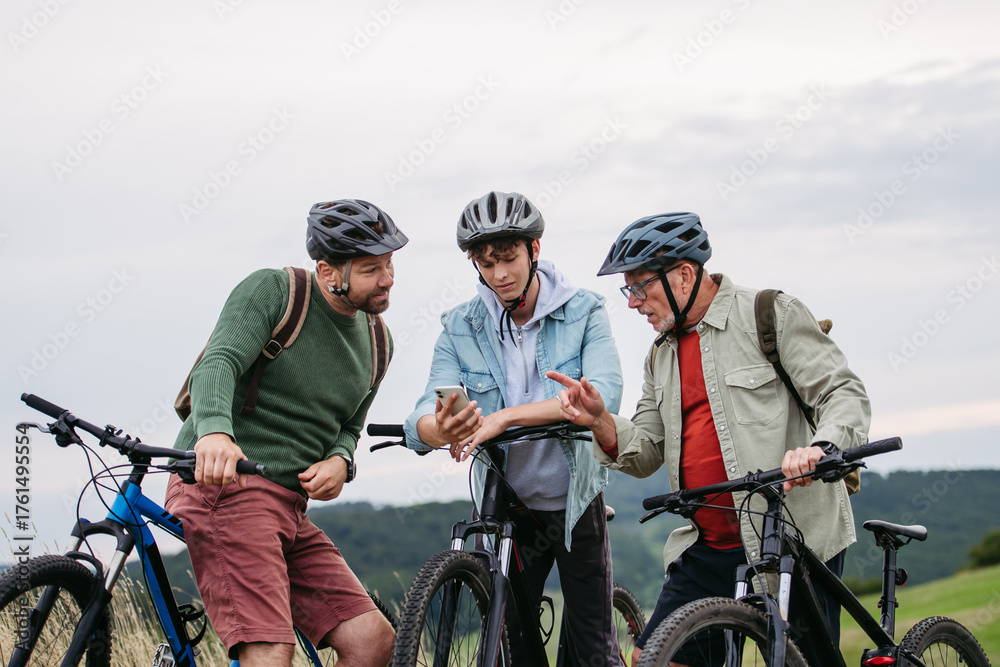 Naklejka premium Grandfather, father and teen boy on cycling trip looking at map in smartphone.