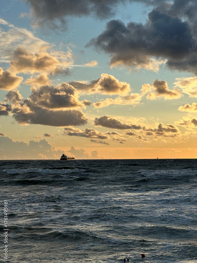 Fototapeta premium Cargo ship on distant horizon at sea during sunset