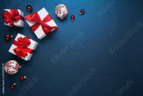 Merry Christmas and Happy Holidays greeting card, frame, banner. New Year. Red and white Christmas decorations and gifts on blue background top view. Winter xmas holiday celebration theme.