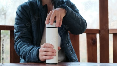 Detailed close-up of a man's hand unscrewing the lid of a white thermos. Ideal 4K video for product, travel, and outdoor lifestyle content.