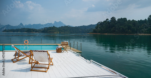 Fototapeta Naklejka Na Ścianę i Meble -  wooden beach chair and coffee table on white raft and swimming pool at waterfront of the open water in natural lake