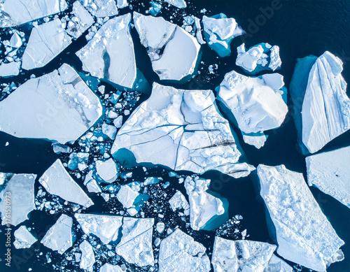 Broken glacier ice pieces floating in deep blue ocean from drone view