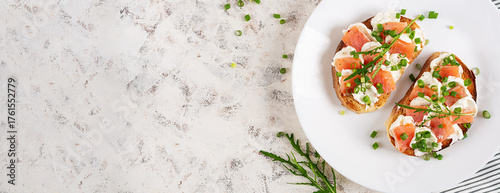 Two open sandwich, toast with salmon, cream cheese, green onions for healthy breakfast on white plate. Top view