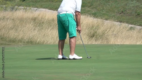 Golfer putting on green during summer game. Man enjoying a summer sport on a luxury golf course. Leisure, hobby, and outdoor recreation concept.