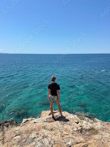 A woman standing on a beautiful tropical island in Madagascar with clear turquoise water. The bright sunlight, blue sky, and crystal-clear ocean create a peaceful and exotic summer atmos