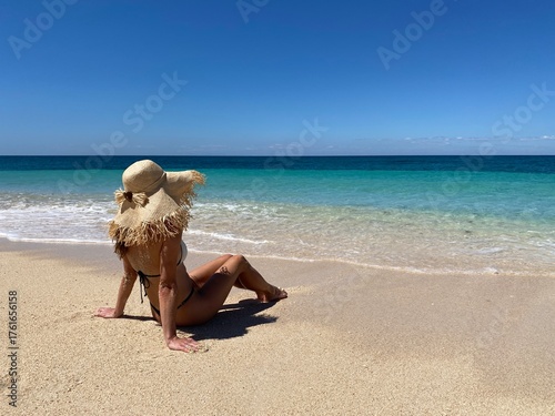 A woman sitting on a beautiful tropical beach in Madagascar with clear turquoise water and white sand. The bright sunlight, blue sky, and crystal-clear ocean create a peaceful and exotic summer 
