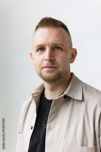 A man with a short haircut and a neutral expression poses in a beige shirt against a white background.