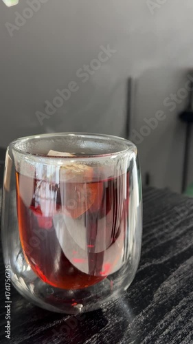 Hot tea being poured from a glass pitcher into a double-walled glass cup, under warm lighting and a dark background.