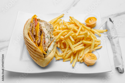 Sandwich triple steak sur une assiette avec des frites et sauces. Spécialité culinaire turque. Restauration rapide.	 Doner kebab.