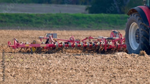 Tractor cultivating dry farmland field with heavy tillage machinery, preparing the soil for the next planting season under bright autumn light.