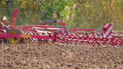 Tractor cultivating dry farmland field with heavy tillage machinery, preparing the soil for the next planting season under bright autumn light.