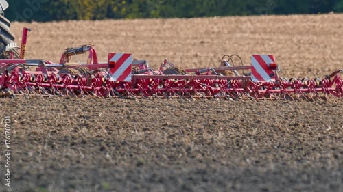 Tractor cultivating dry farmland field with heavy tillage machinery, preparing the soil for the next planting season under bright autumn light.