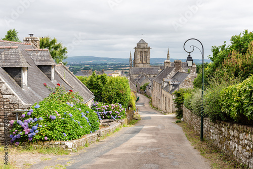 Picturesque street of Locronan with granit houses and hydrangea garden leading to the Saint Ronan Cathedral, int the Finistere department of Brittany, France.