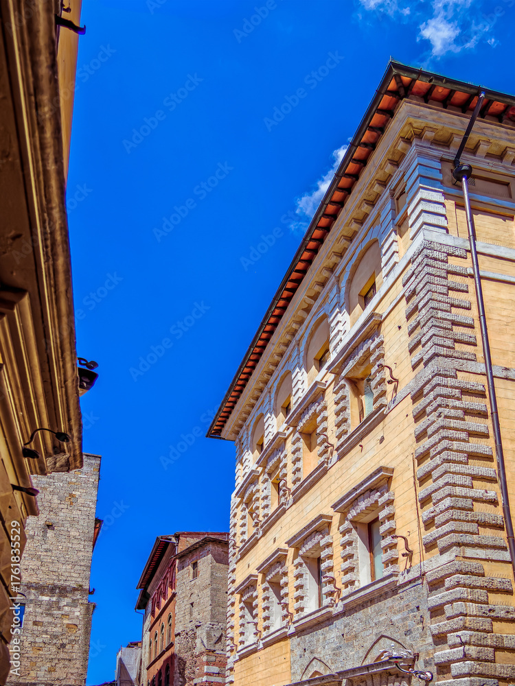 Fototapeta premium Classic vintage buildings stand elegantly under a vibrant blue sky in Siena, Tuscany, Italy, showcasing intricate stone facades, arched windows, and historic charm.