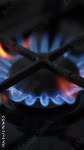 A side-view slow-motion shot of a black gas stove igniting. Elegant blue and red flames dance on the burner in a cinematic close-up.