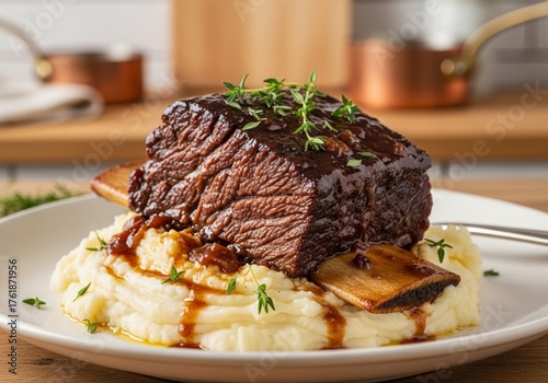 Tender Beef Short Ribs Served Over Creamy Mashed Potatoes, Garnished with Fresh Thyme, Warm and Inviting Culinary Experience for Food Enthusiasts and Home Cooks, Blurred Kitchen Background