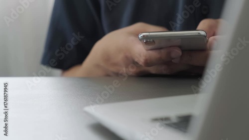 man using smartphone and laptop with relaxed posture focused on screen and hands typing and browsing mobile device technology in calm indoor setting