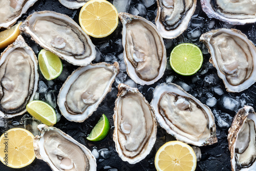 Wallpaper Mural Fresh raw oysters on ice background texture, overhead flat lay view on black slate, with lemon and lime Torontodigital.ca