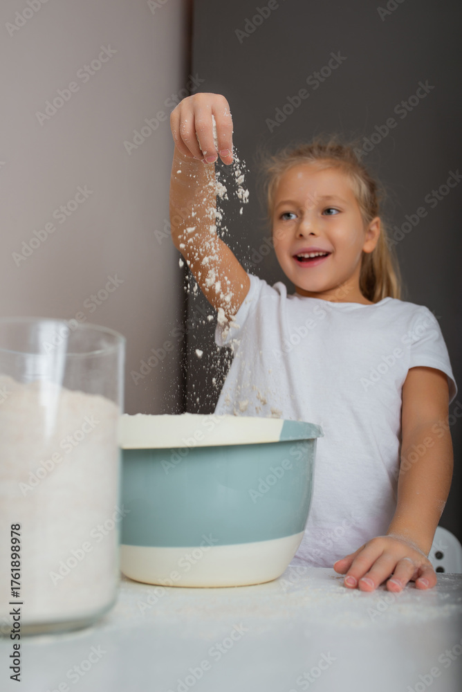 Fotografie Little girl playing with flour in the kitchen while baking.