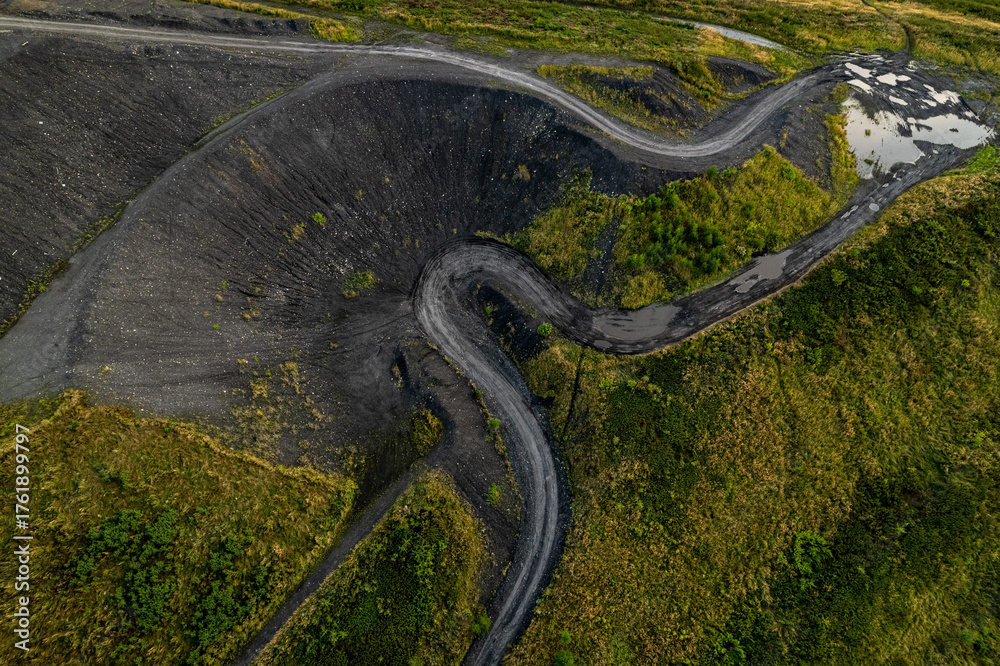 Naklejka premium Winding asphalt road through coal mining waste dump aerial view Rybnik Poland horizontal black slag heap green vegetation industrial landscape