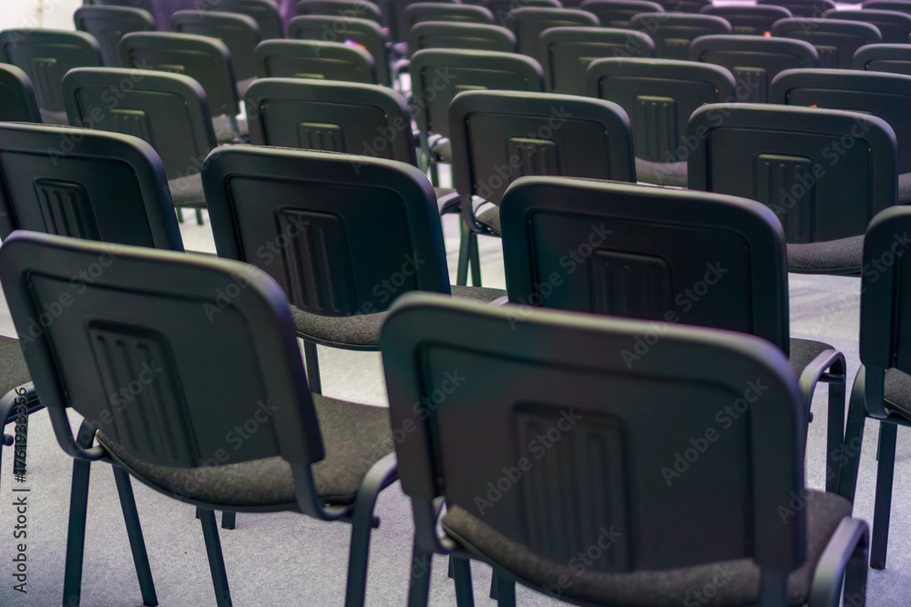 Naklejka premium multiple rows of empty black chairs in a dimly lit conference hall or auditorium concept of corporate meeting, seminar presentation, training event