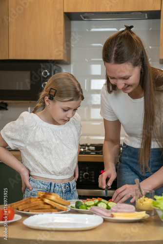 Mother and daughter bonding in a modern kitchen, preparing fresh homemade sandwiches together with various ingredients, learning cooking skills and enjoying family togetherness. Vertical photo