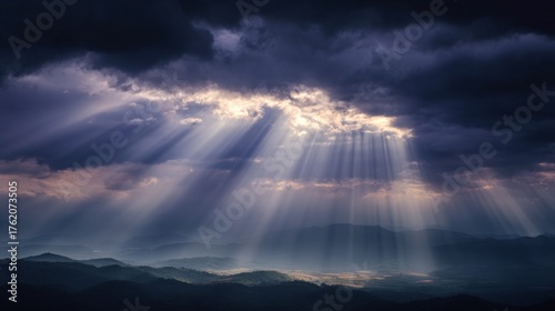 Dramatic landscape of dark storm clouds parting to reveal sun rays breaking through onto distant layered mountain ridges