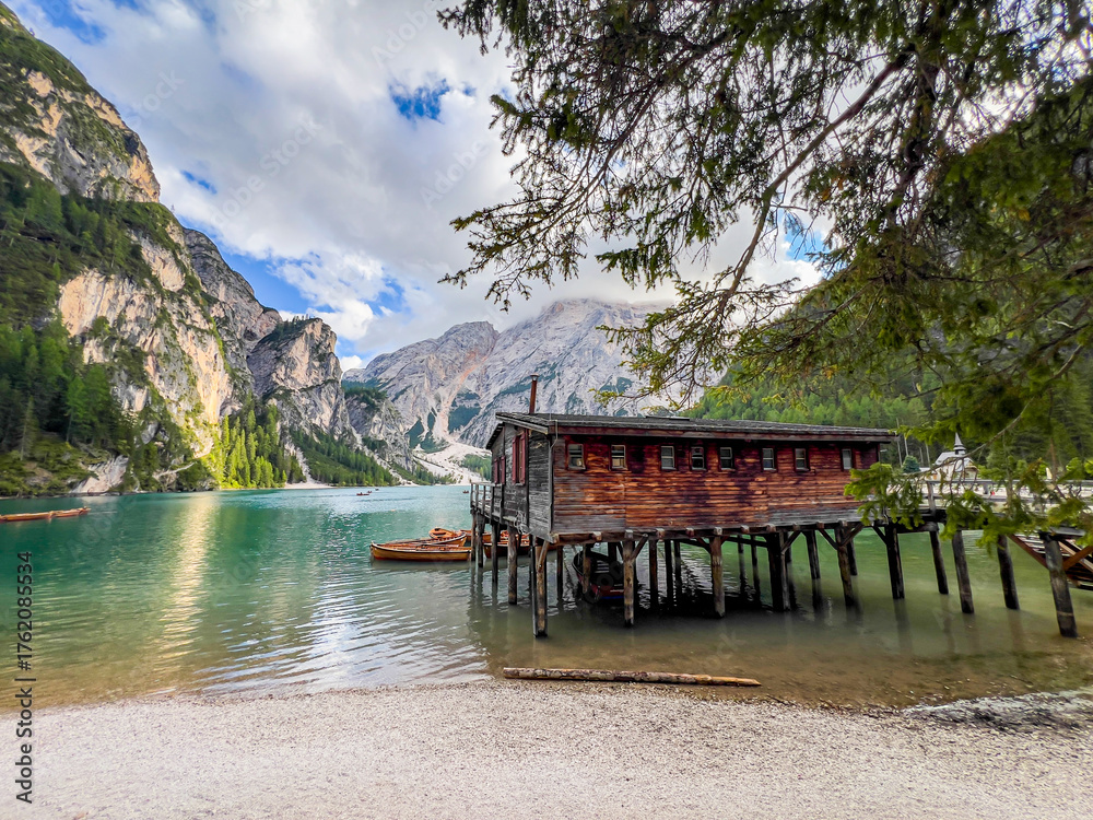 Naklejka premium Lago di Braies or Lake Braies crystal blue lake with wooden rowing boats in Italian Dolomites. Mountain forest lake in Italian alps Dolomites South Tyrol. Woden cabin hut and pontoon above the lake.