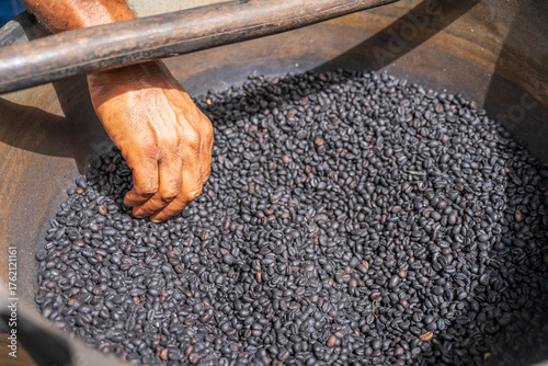 A hand takes coffee beans from a bowl, inside pile of  dark roasted coffee beans outdoor at sunny day, Suitable for marketing or business purposes.close-up top view