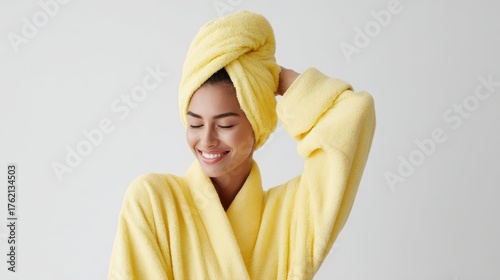 Pleased woman in yellow bathrobe, drying her hair after bath, cheerful expression, studio shot on white backdrop