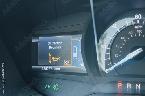 Close-up of a modern car dashboard, displaying an Oil Change Required warning light and message. Digital gauge cluster showing speedometer, fuel and battery status with high mileage